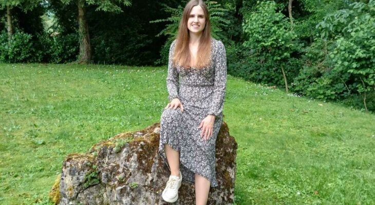 Die Autorin des Blogs sitzt in einem geblümten Kleid auf einem Felsen in der Natur.